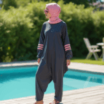 a woman standing poolside on a wooden deck wearing a modern anthracite colored modest swimwear set sojveswqclsdp
